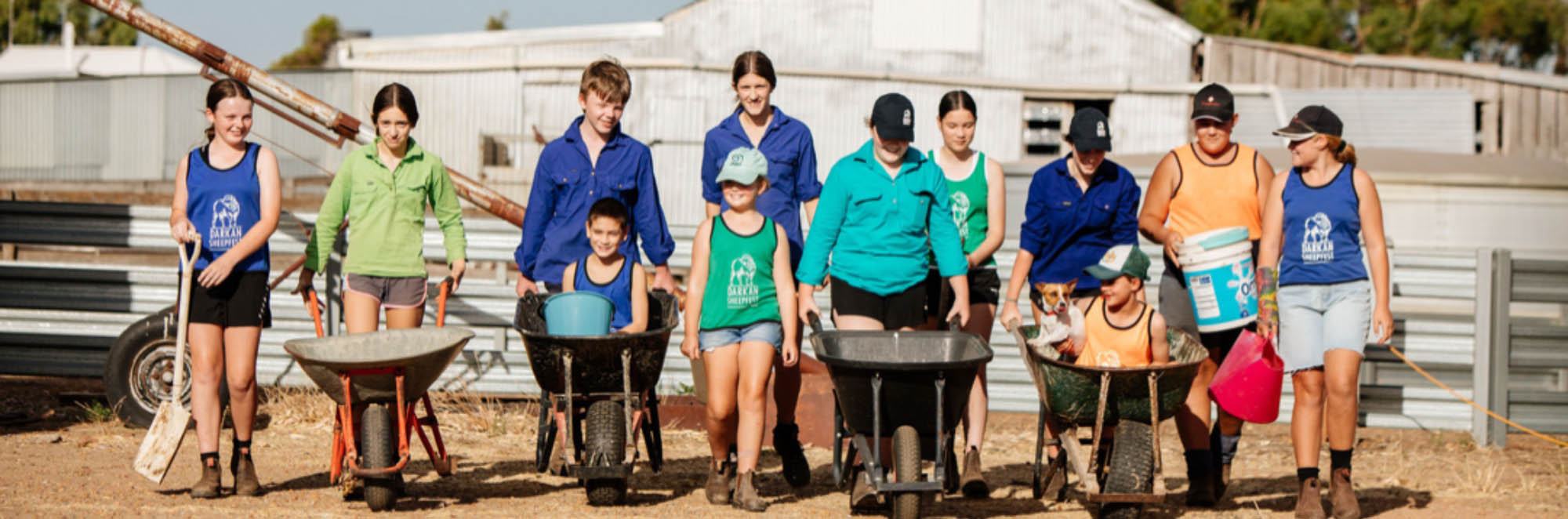 photo of a group of adults and children in colourful farm shirts with wheelbarrows for collecting sheep poo