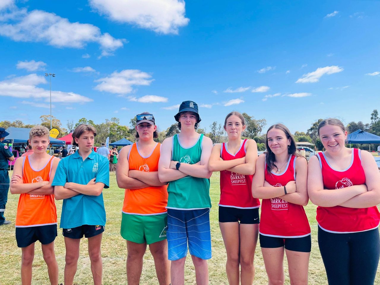 seven young teenagers standing with arms crossed and looking at the camera. They are mostly wearing brightly coloured shearing singlets and shorts.